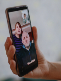 Una mano sosteniendo un teléfono celular con un bebé en una videollamada con miembros de la familia